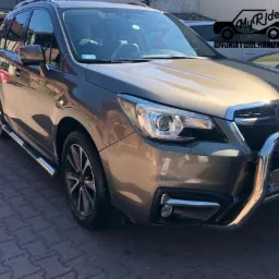 Brązowy samochód SUV, Subaru Forester, wycierany z przodu przez osobę w rękawicach, widoczne logo firmy detailingowej w rogu.