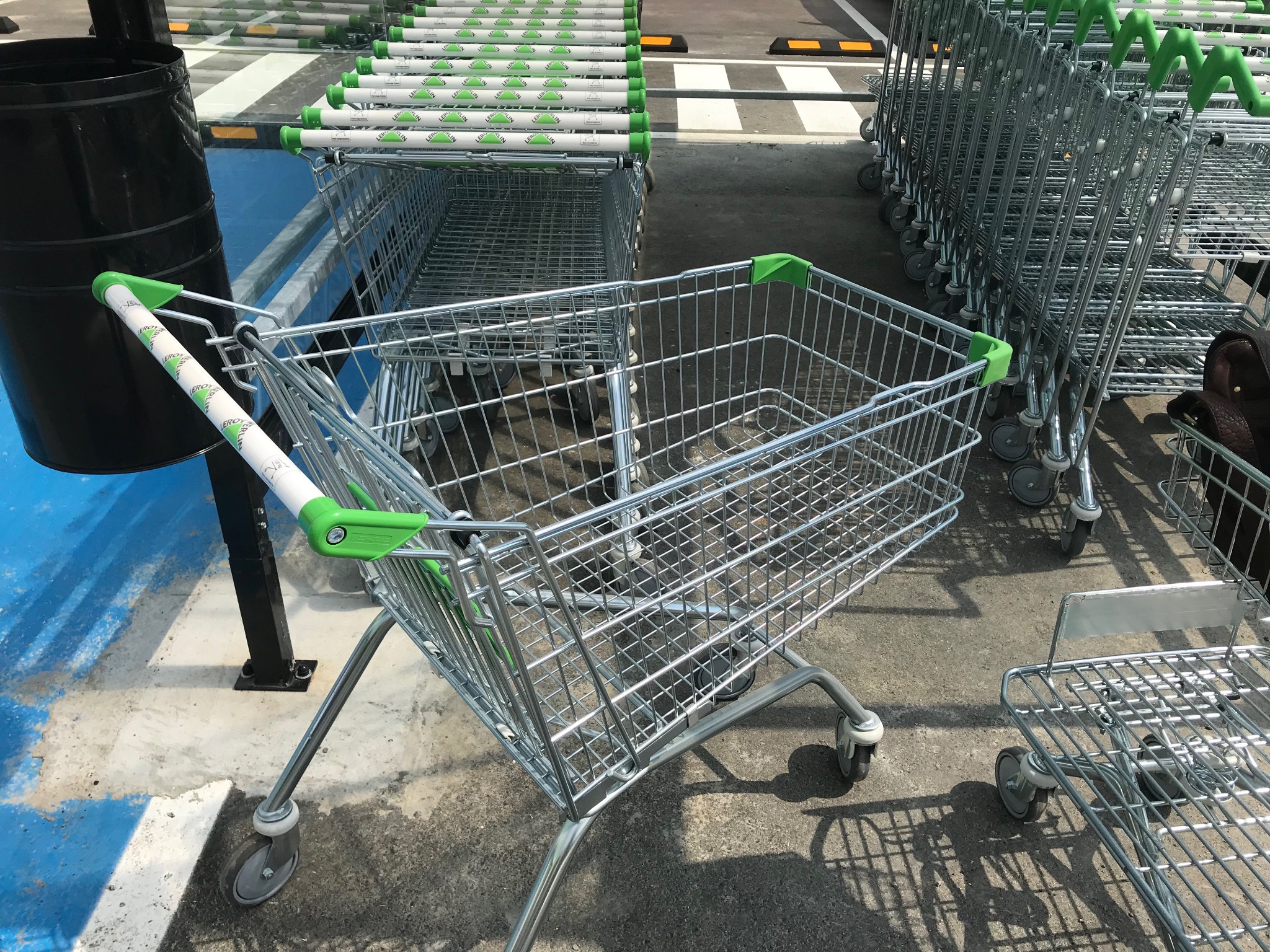 Rząd metalowych wózków sklepowych z zielonymi uchwytami, ustawionych na zewnątrz na parkingu sklepu.