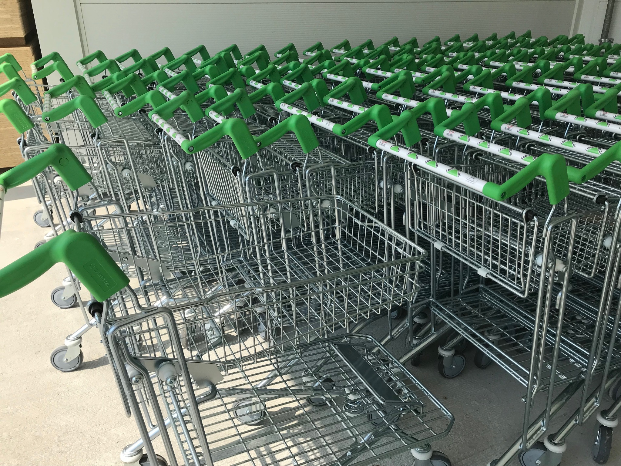 Rząd pustych wózków sklepowych z zielonymi uchwytami, ustawionych jeden za drugim, widok z boku.