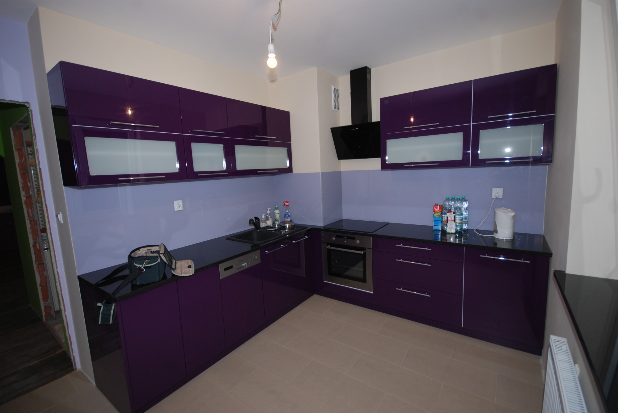 Fioletowa, nowoczesna kuchnia z czarnym blatem, jasnymi płytkami i otwartą torbą na blacie.