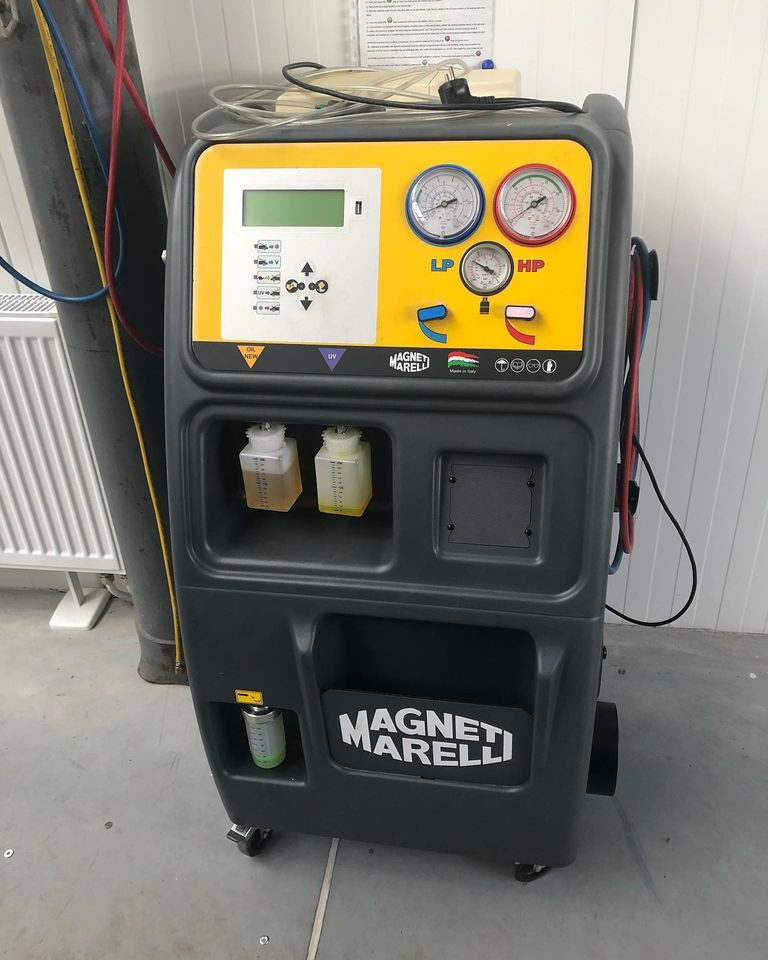 Stacja do obsługi klimatyzacji samochodowej Magneti Marelli z manometrami, wyświetlaczem LCD, pojemnikami na olej i UV, oraz widocznymi przewodami w warsztacie.