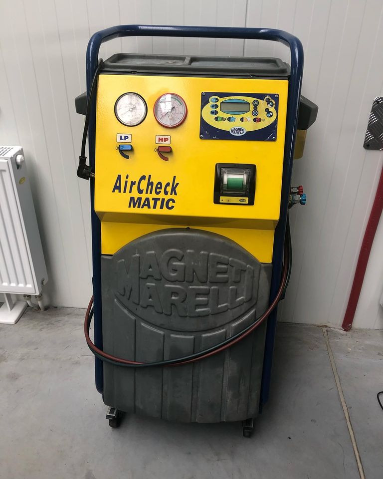 Żółto-szare urządzenie AirCheck MATIC firmy Magneti Marelli na kółkach, z manometrami i wyświetlaczem, służące do obsługi klimatyzacji samochodowej, stojące w warsztacie.