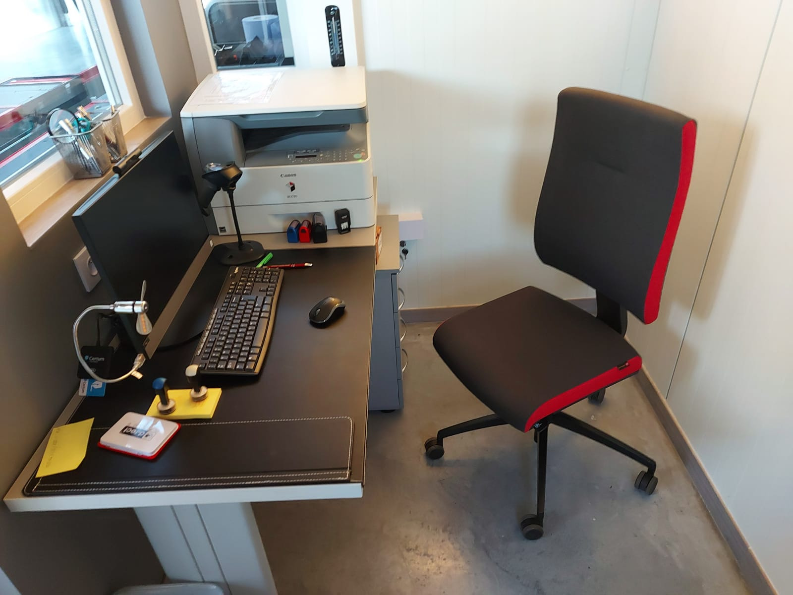 Stanowisko biurowe w Zalesiu z biurkiem, komputerem, drukarką i krzesłem z czerwonymi akcentami.
