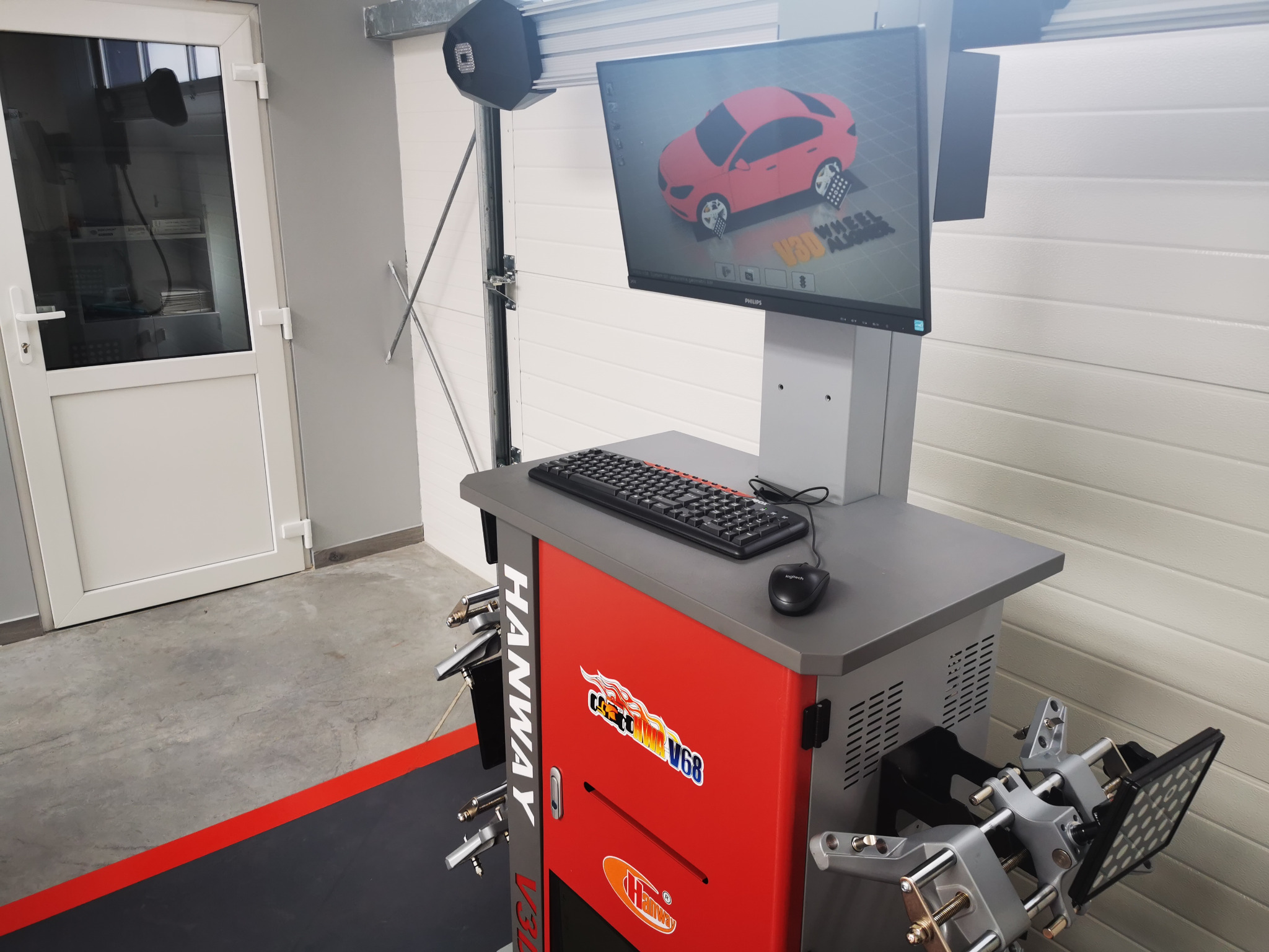 Stanowisko do geometrii kół z widocznym monitorem prezentującym model samochodu z naniesionymi punktami pomiarowymi, klawiaturą, myszką oraz elementami mocującymi do kół pojazdu.