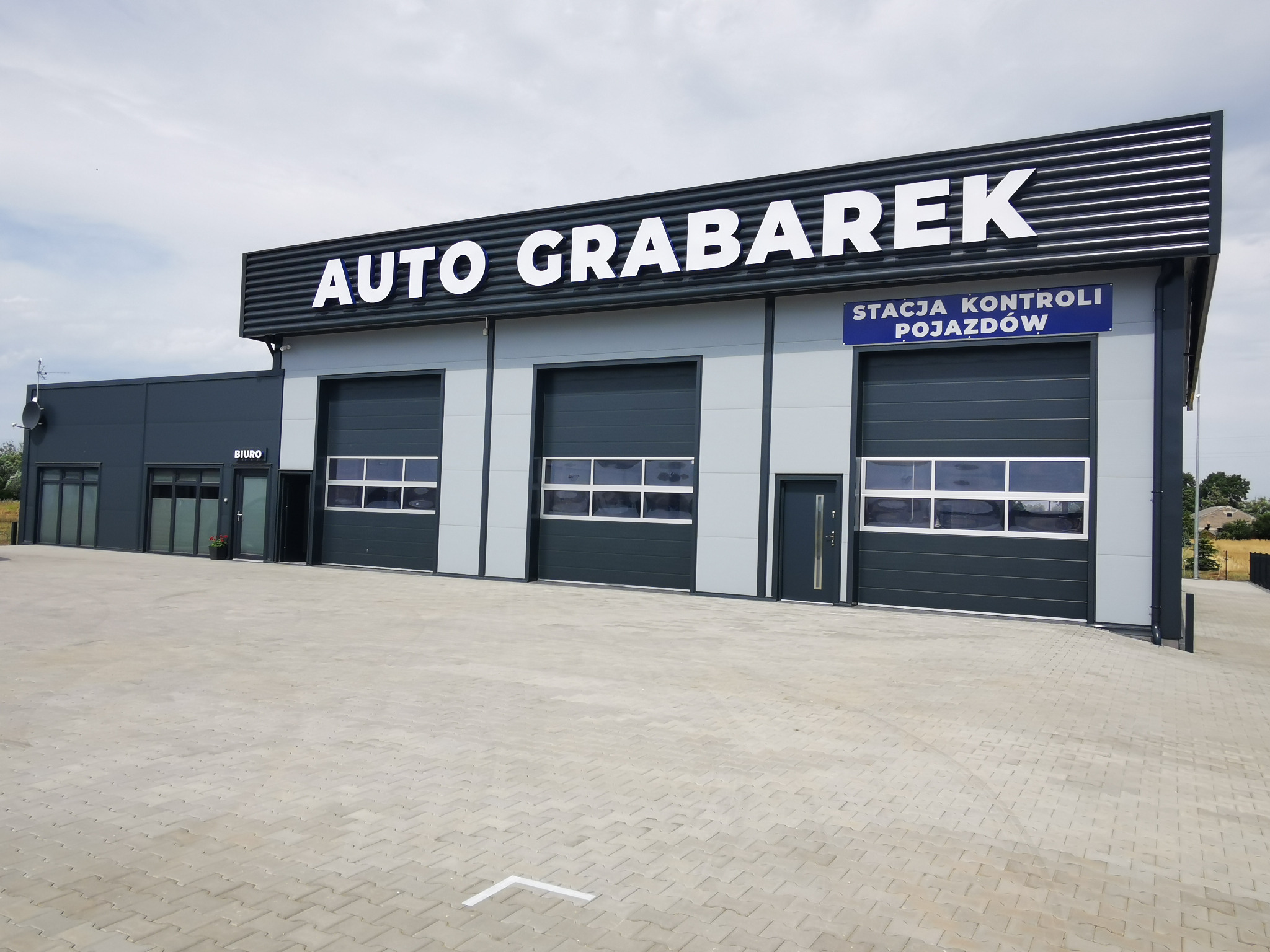 Budynek warsztatu samochodowego Auto Grabarek z trzema bramami garażowymi i napisem Stacja Kontroli Pojazdów