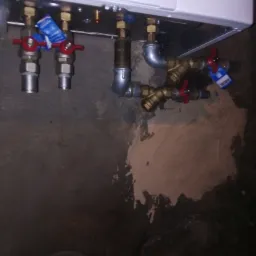 Podwieszony piec gazowy ecoTEC pure z podłączonymi rurami miedzianymi i zaworami z czerwonymi pokrętłami, widoczne nieestetyczne ślady po montażu na ścianie.