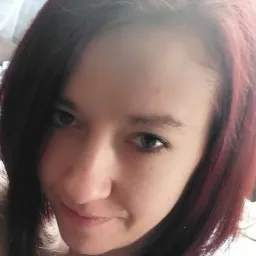 Portret młodej kobiety z ciemnymi włosami z czerwonymi refleksami, uśmiechającej się lekko, z bliska.