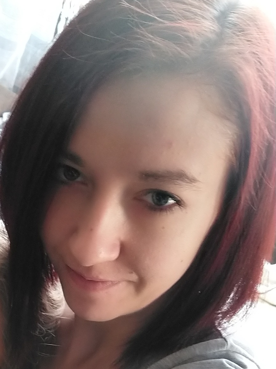 Portret młodej kobiety z ciemnymi włosami z czerwonymi refleksami, uśmiechającej się lekko, z bliska.