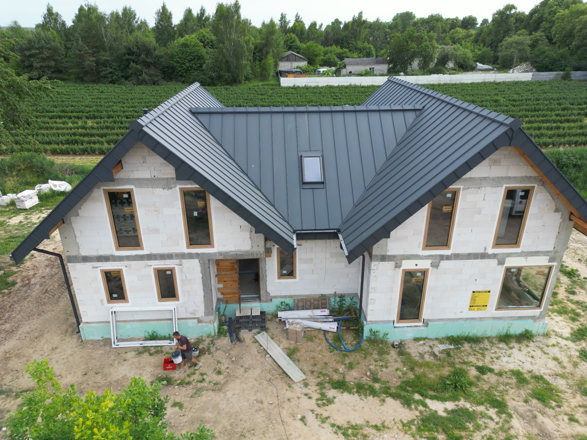 Dom w stanie surowym otwartym z zamontowanym, szarym dachem z blachy na rąbek stojący i oknem dachowym; widoczne przygotowania do dalszych prac wykończeniowych.
