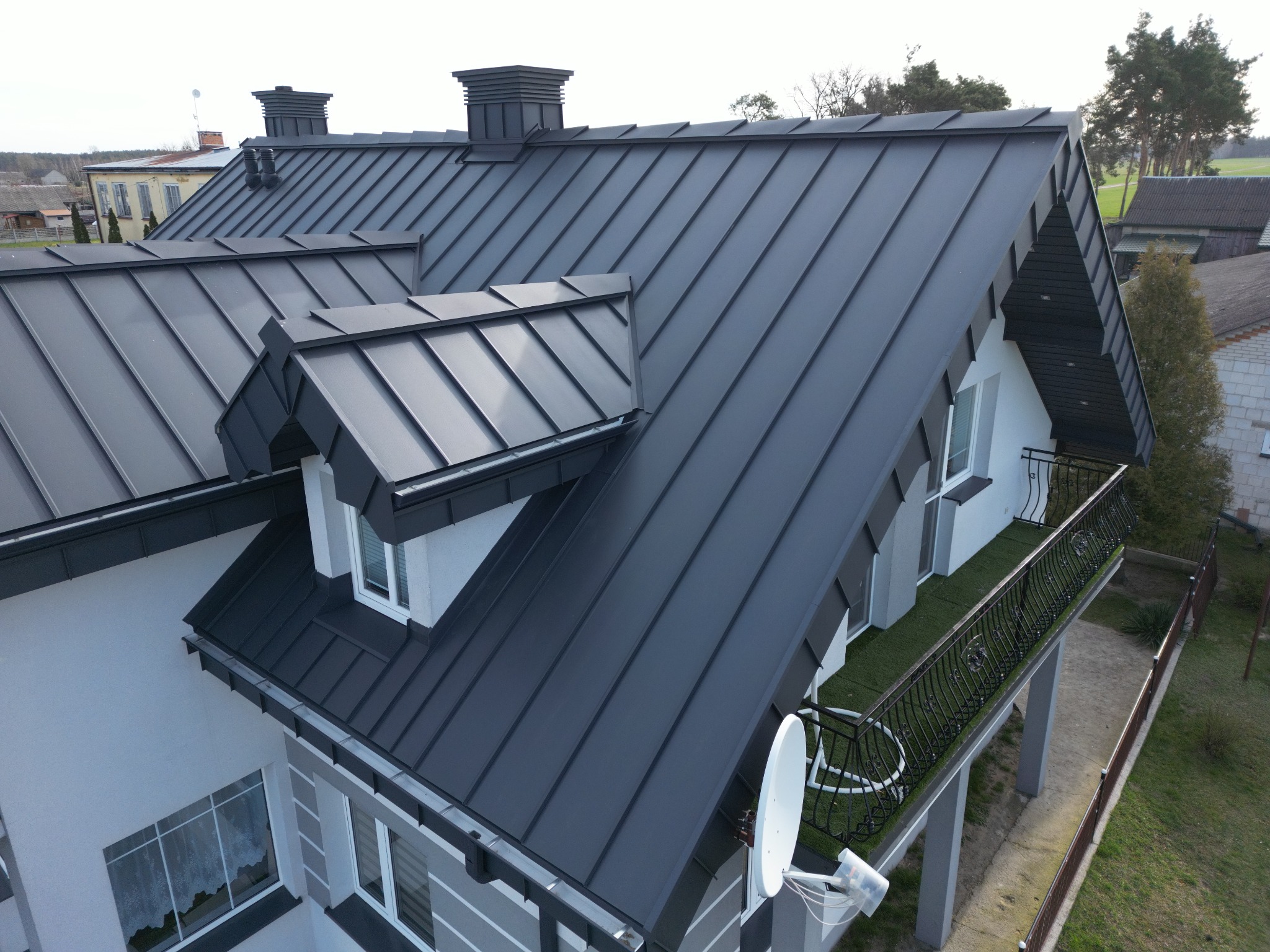 Nowoczesny dom z ciemnoszarym, metalowym pokryciem dachowym, widok z góry, z kominami i lukarną.