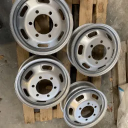 Cztery stalowe felgi samochodowe po renowacji, leżące na drewnianej palecie. Felgi mają świeżą, srebrną powłokę.