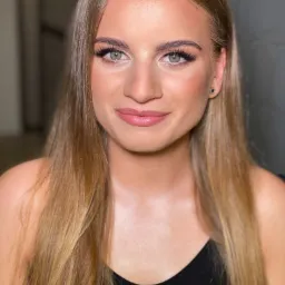 Portret młodej kobiety z delikatnym, naturalnym podkreśleniem oczu i ust, długie blond włosy, czarny top, widoczne kolczyki w uszach.