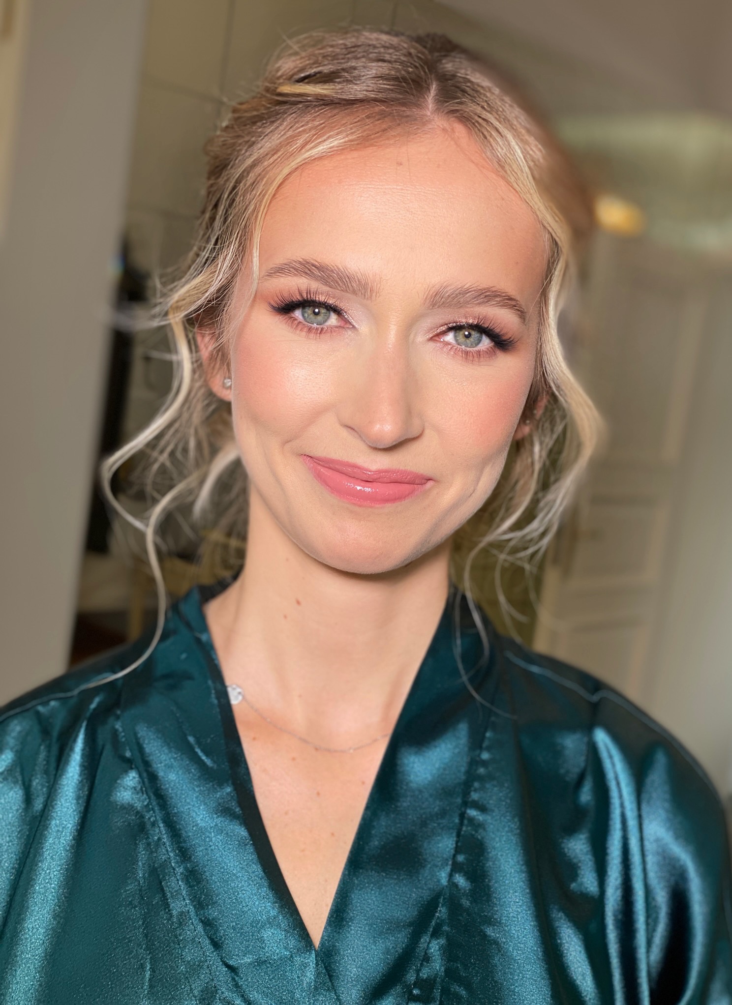 Portret uśmiechniętej blondynki z delikatnym, rozświetlającym make-upem, w szmaragdowym szlafroku.