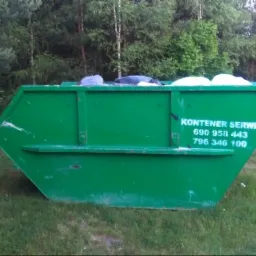 Zielony kontener napełniony odpadami stoi na trawie, z widocznym napisem 'Kontener Serwis' i numerami telefonów, w tle drzewa.