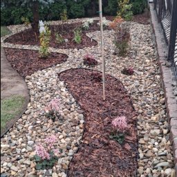 Twój Ogrodnik - Ogród z kamienną ścieżką i korą, obrzeża z tworzywa. W tle iglaki, drzewo kuliste i metalowe ogrodzenie. Dekoracyjny układ kamieni i roślin.