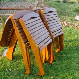 Trzy złożone drewniane leżaki ogrodowe ustawione na trawniku w słoneczny dzień.