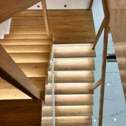 Paweł Juraszek - Nowoczesne schody z jasnego drewna z podświetleniem LED, widok z góry. Minimalistyczny design, marmurowa podłoga w tle. Ujęcie podkreśla precyzję wykonania.