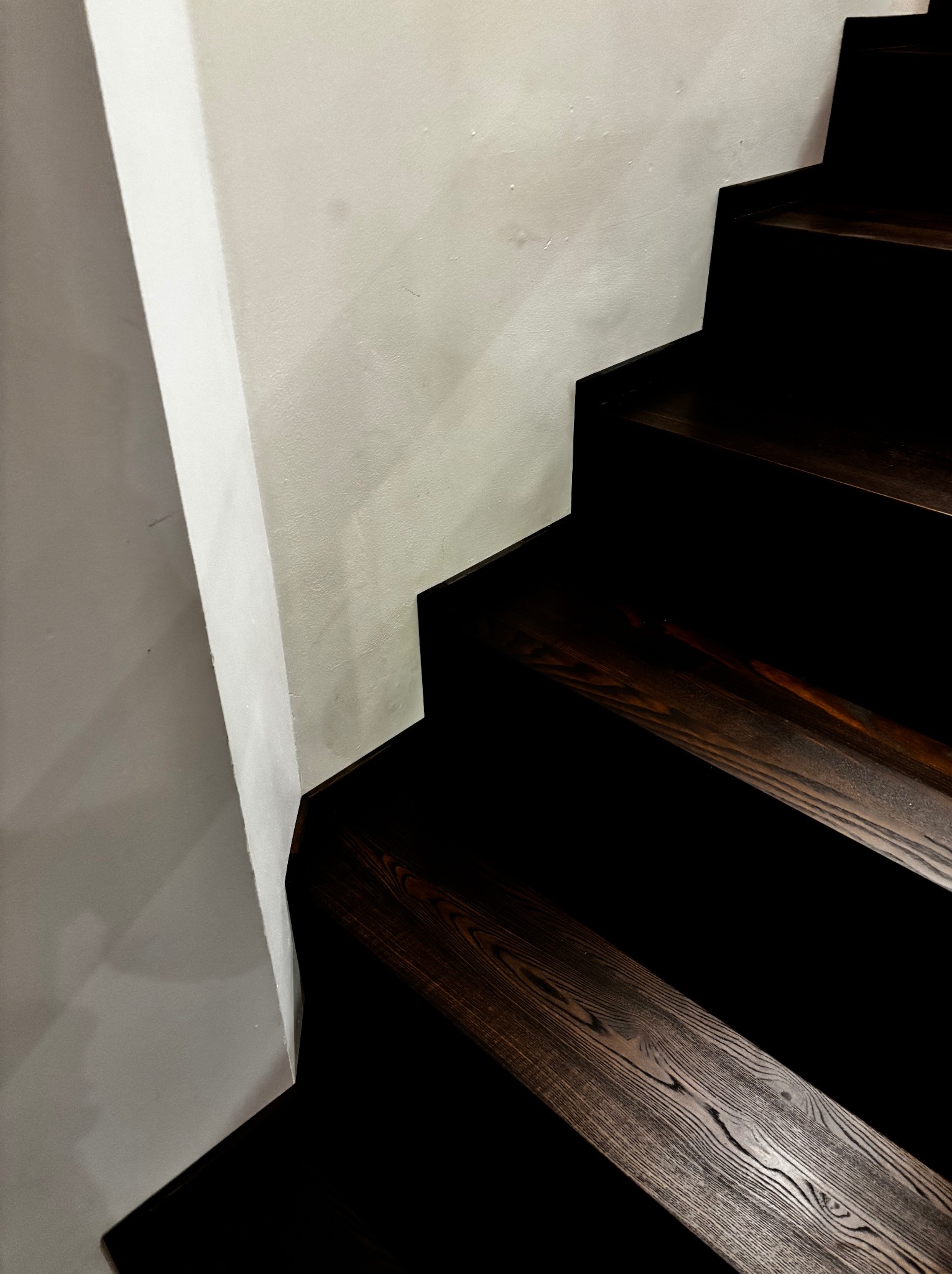 Ciemne stopnie schodów z drewna, widoczne z bliska, kontrastują z białą ścianą. Realizacja w Dzierżoniowie, detale wykończenia.