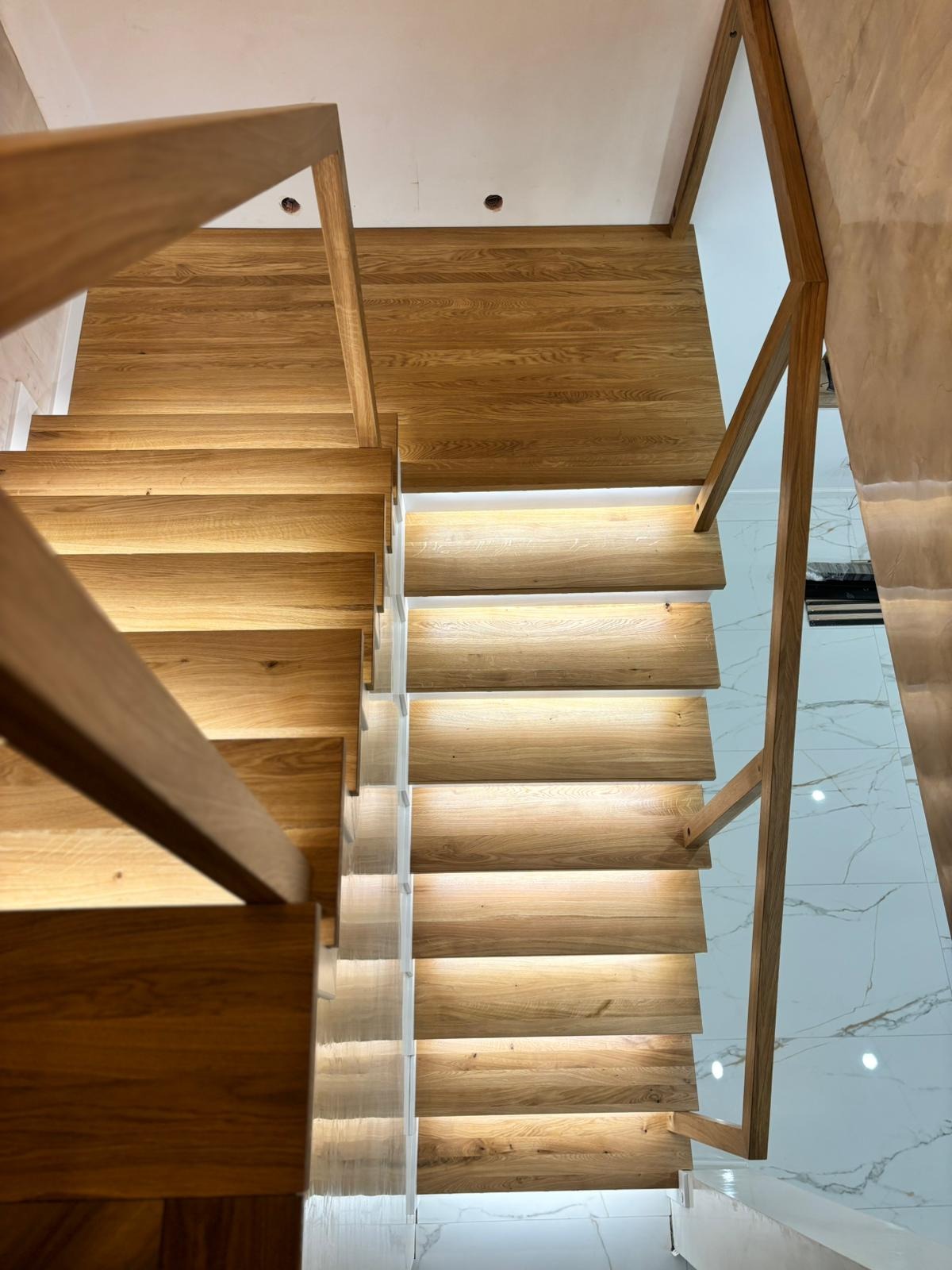 Nowoczesne schody z jasnego drewna z podświetleniem LED, widok z góry. Minimalistyczny design, marmurowa podłoga w tle. Ujęcie podkreśla precyzję wykonania.