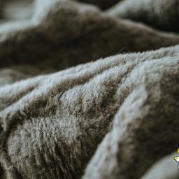 KRYSTA Andrzej Pająk i Krystyna Pająk s.c. - Szczegółowe ujęcie szarej, miękkiej tkaniny pościelowej z logo firmy z Bielska-Białej w prawym dolnym rogu.