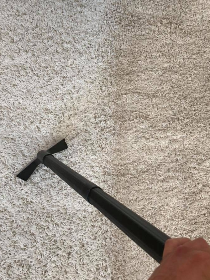 Dywan w trakcie czyszczenia: widoczna wyraźna różnica między wyczyszczoną, jaśniejszą lewą stroną a brudną, ciemniejszą prawą stroną. W kadrze fragment urządzenia czyszczącego z czarną rurą.