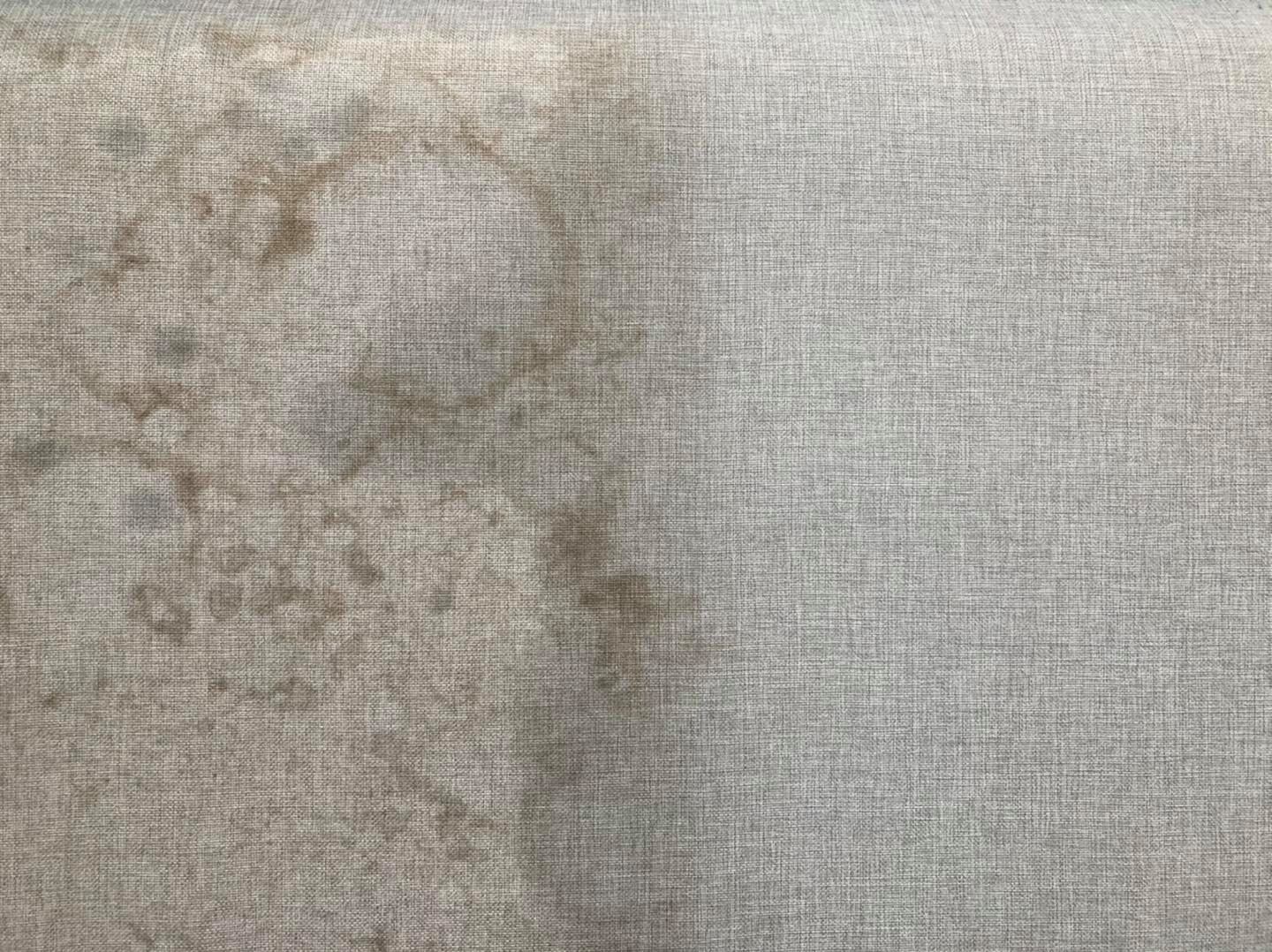 Fragment szarej tapicerki narożnika, po lewej stronie widoczne liczne, ciemne plamy przed czyszczeniem, po prawej stronie czysta, odświeżona tkanina po zabiegu.