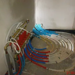 Rozdzielacz ogrzewania podłogowego z rurami PEX w kolorach czerwonym, niebieskim i białym, ułożonymi w pętle na surowej posadzce, przed wylaniem wylewki.