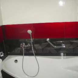 Wykończona łazienka z wanną, chromowaną armaturą i ścianami wyłożonymi błyszczącymi płytkami w kolorach białym, czerwonym i czarnym z geometrycznym wzorem.