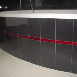 Obudowa wanny wykończona czarnymi, pionowymi płytkami z poziomym pasem czerwonych akcentów, jasna podłoga z płytek.