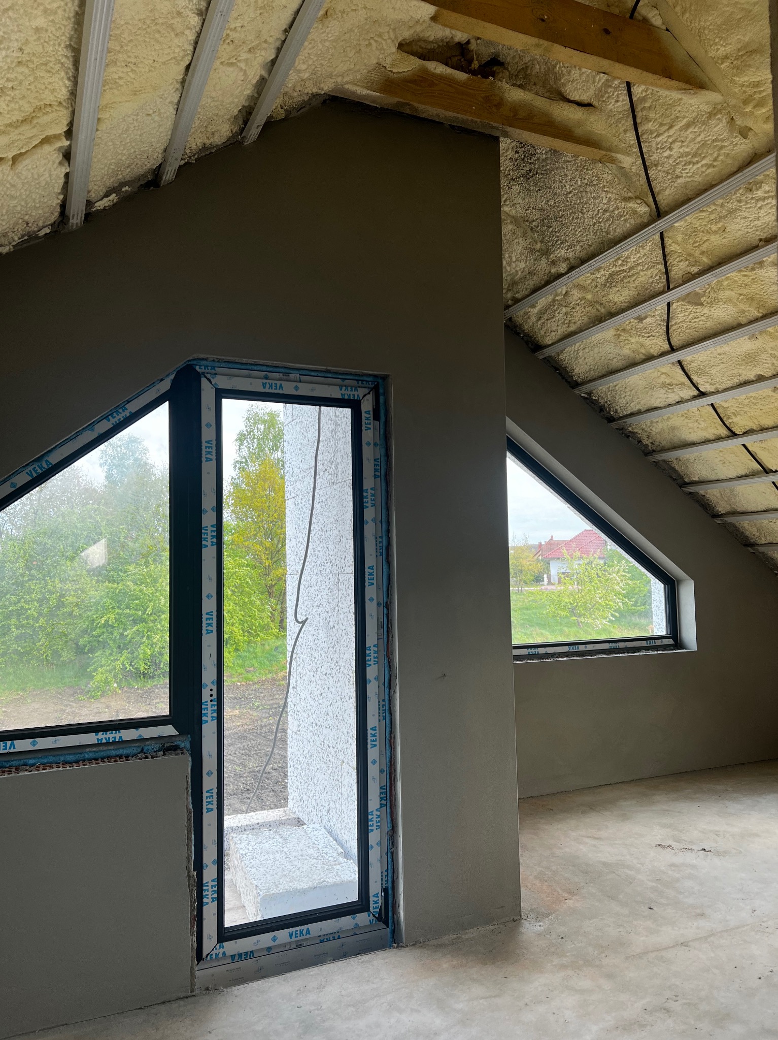 Poddasze w trakcie wykańczania, ściany po tynkowaniu maszynowym, widoczne okna dachowe i izolacja pianą PUR na poddaszu, profile okienne z logo VEKA.