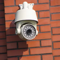 Kamera monitoringu z diodami IR, zamontowana na ceglanej ścianie budynku, widok z dołu.