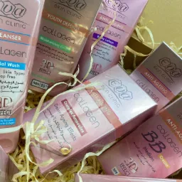 Zestaw kosmetyków EVA Skin Clinic z kolagenem, w odcieniach różu i beżu, ułożony w ozdobnym pudełku wypełnionym papierową wełną. Widoczne różne produkty: kremy, balsamy, ampułki i żel do mycia twarzy.