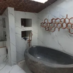 Niedokończona łazienka z kamienną wanną, złotą armaturą, marmurowymi płytkami i drewnianym sufitem z oknem dachowym.