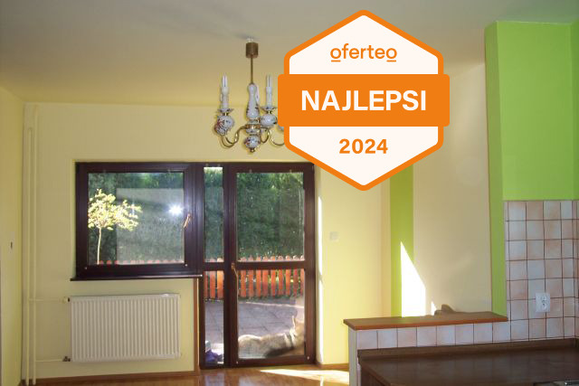 Wnętrze pokoju po odświeżeniu, z jasnymi ścianami w odcieniach żółci i zieleni, widoczne okno balkonowe z brązową ramą, grzejnik oraz fragment kuchni z kafelkami. Na zdjęciu naklejka Oferteo...