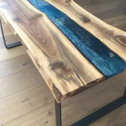 Stolik kawowy z blatem z naturalnego drewna z żywicą epoksydową w kolorze błękitu, osadzony na czarnych, metalowych nogach, widoczny na drewnianej podłodze.