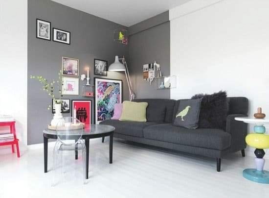 Nowoczesny salon z szarą ścianą, ciemną sofą z poduszkami, okrągłym stolikiem z przezroczystym krzesłem i lampą podłogową