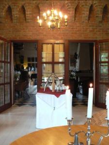 Wnętrze ośrodka wypoczynkowego z widoczną ceglaną ścianą z łukami, otwartymi drewnianymi drzwiami prowadzącymi do dalszej części obiektu, dekoracyjną lampą sufitową, stołem nakrytym białym obrusem...