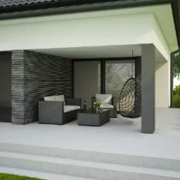 Zadaszony taras z meblami ogrodowymi z rattanu, wiszącym fotelem, butelką wina i szklankami na stoliku kawowym, wykończony płytkami w jasnym odcieniu szarości i cegłą klinkierową w ciemnym odcieniu...