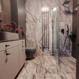 kajbud usługi remontowo-budowlane - Nowoczesna łazienka z marmurową podłogą i ścianami, szklaną kabiną prysznicową oraz grafitową toaletą i umywalką. Minimalistyczny design i eleganckie wykończenie.