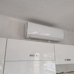 KOVALINSTAL JACEK KOWALIK - Biały klimatyzator Sinclair zamontowany nad błyszczącymi szafkami w Kurzelowie. Widoczne niedociągnięcia malarskie na ścianie.