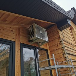 KOVALINSTAL JACEK KOWALIK - Montaż klimatyzacji zewnętrznej na drewnianej elewacji domu z widoczną drabiną, wykonany pod kątem, prezentujący detale instalacji i otoczenia.