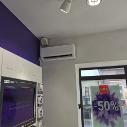 KOVALINSTAL JACEK KOWALIK - Klimatyzator Rotenso zamontowany na ścianie w pomieszczeniu z fioletowym akcentem kolorystycznym. Widoczny ekran telewizora i szyba z napisem 'SALE -50%'.