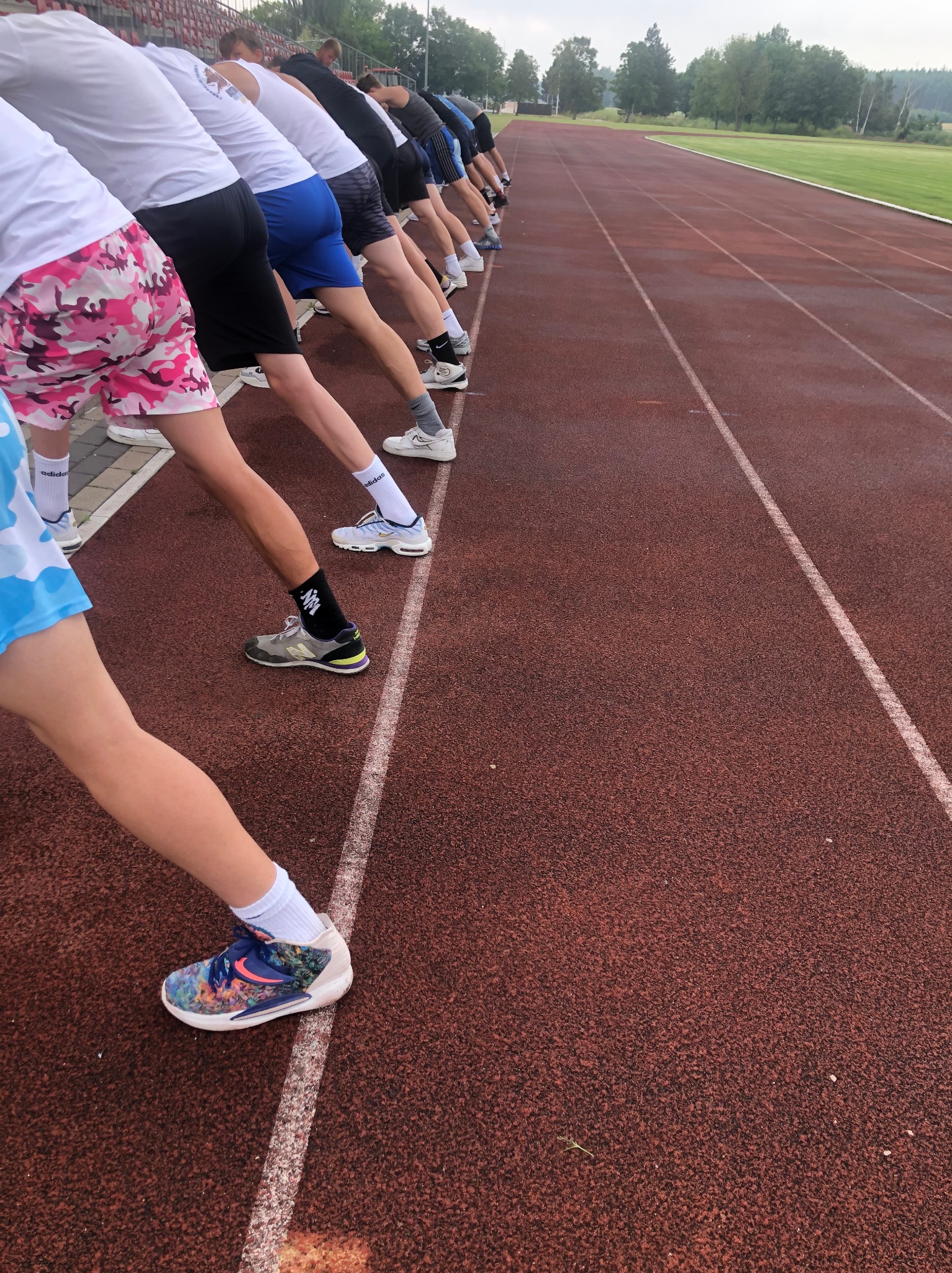 Grupa sportowców rozciąga mięśnie na bieżni w Bydgoszczy, przygotowując się do treningu, widoczne różnorodne stroje sportowe i obuwie.