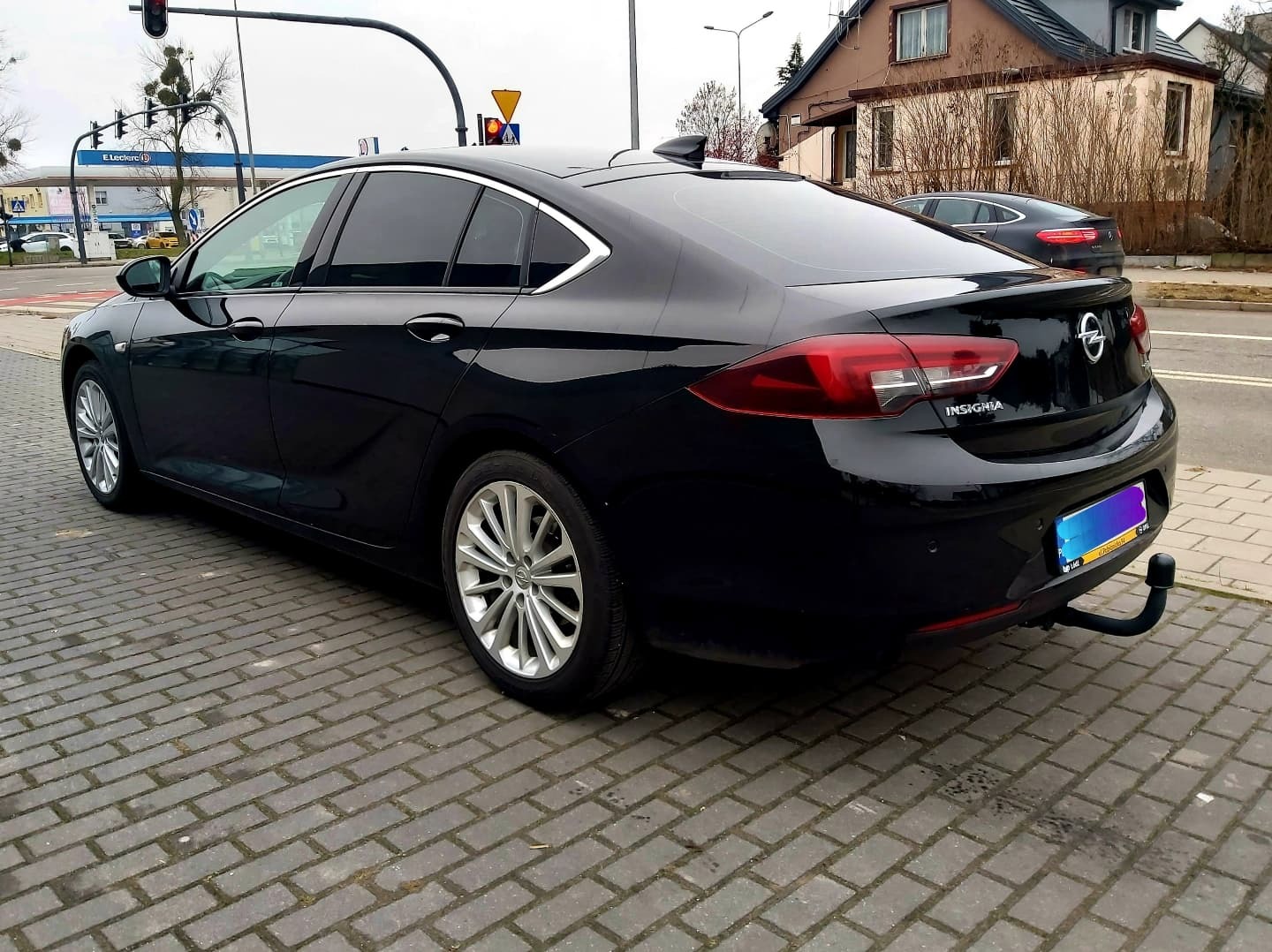 Czarna Opel Insignia po zabiegu przyciemniania szyb, zaparkowana na brukowanej ulicy w miejskiej scenerii, z widocznym hakiem holowniczym.