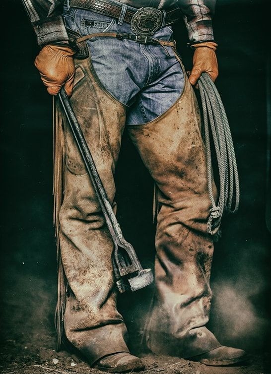 Kowboj w skórzanych ochraniaczach trzyma rozgrzane żelazo do znakowania bydła i lasso.