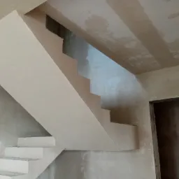 Surowe schody betonowe po nałożeniu gładzi, widoczne ślady prac na ścianach i suficie, przygotowane do dalszego wykończenia.