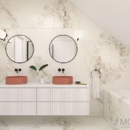 Nowoczesna łazienka na poddaszu z marmurowymi płytkami, dwoma okrągłymi lustrami w czarnych ramach, dwoma umywalkami w kolorze terakoty i białą szafką z ryflowanymi frontami.