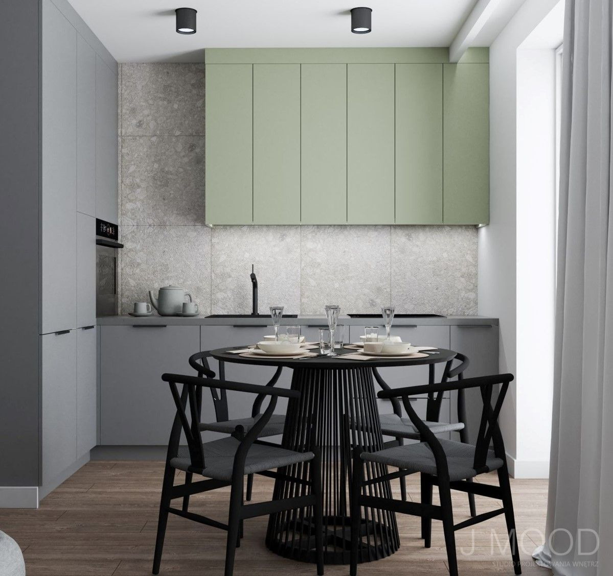 Nowoczesna kuchnia w odcieniach szarości i pistacjowej zieleni z okrągłym, czarnym stołem i czterema krzesłami typu Wishbone, nakryty do posiłku, z widocznym fragmentem zasłony.