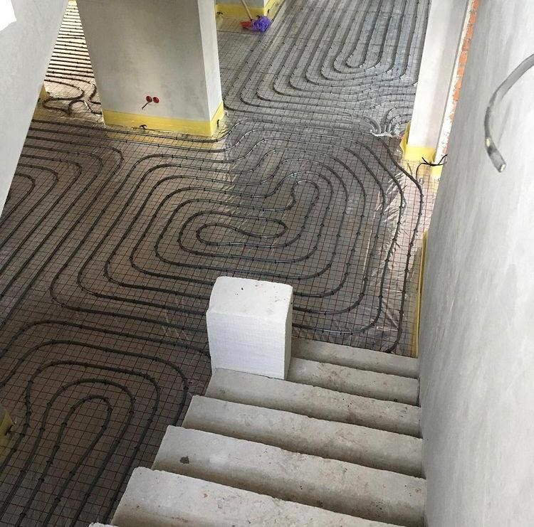 Montaż rur na siatce pod system ogrzewania podłogowego w surowym wnętrzu, widok z góry ze schodów.