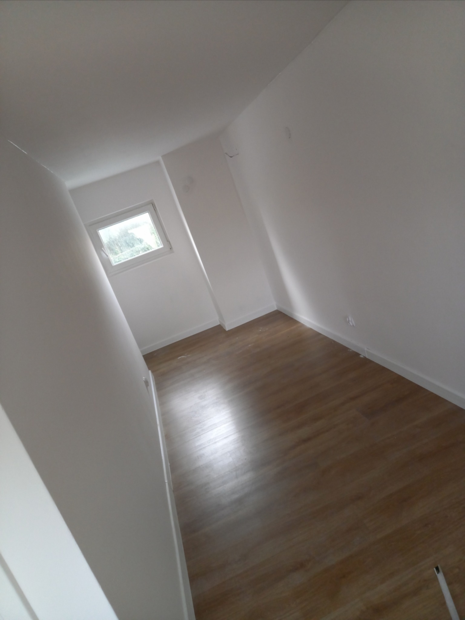 Wnętrze świeżo wykończonego pokoju z panelami podłogowymi i białymi ścianami po malowaniu, widoczne niedoskonałości wykończenia przy listwach przypodłogowych.